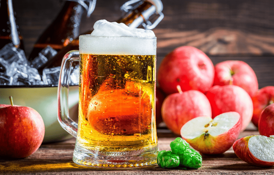 Cider poured into a glass mug beside fresh apples